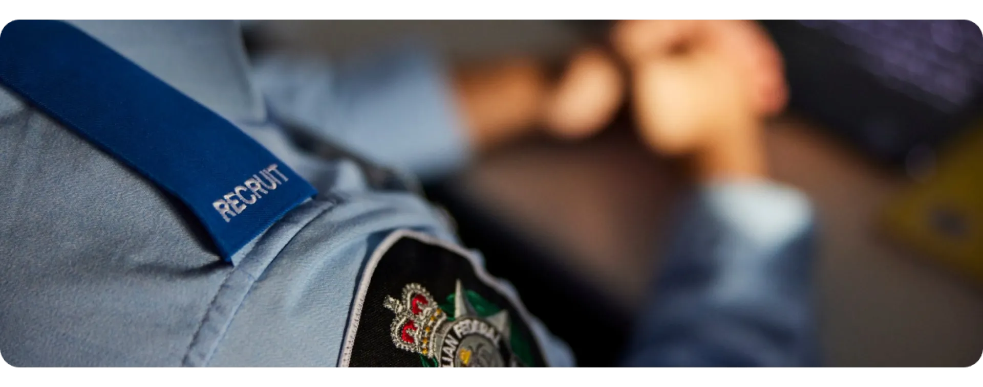 Close-up of a uniform shirt with a blue strap and a badge, hands resting in the background.