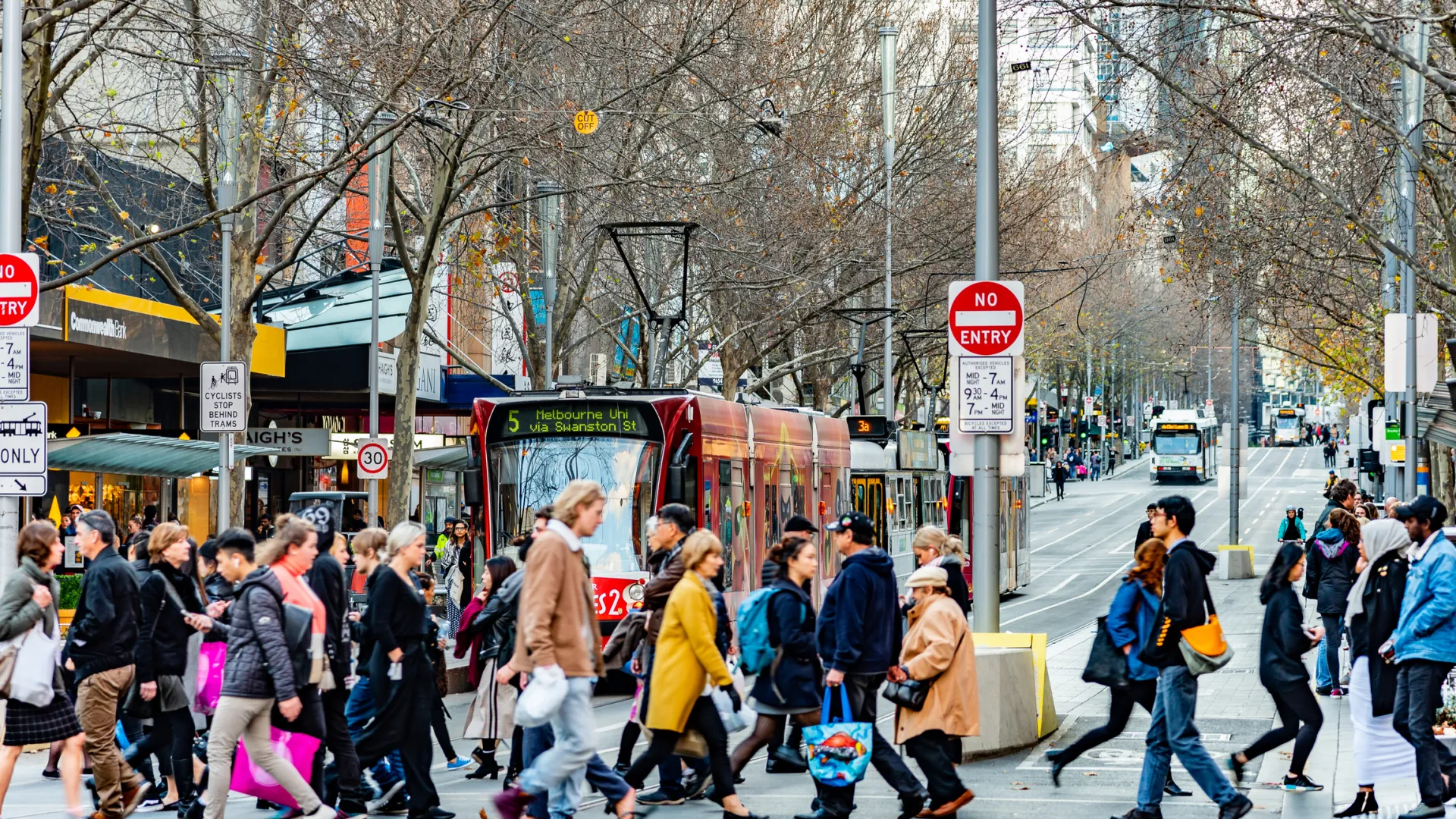 Busy city street with diverse pedestrians crossing, bus in the background, urban setting.
