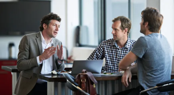 3 guys talking at a desk in an office