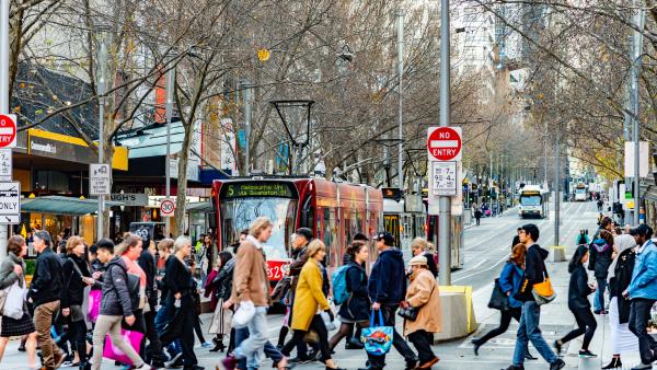 Busy urban street with pedestrians crossing and a bus in the background.